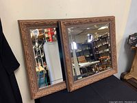 Two square wall mirrors displayed side by side showing detailed carved wooden frames and beveled mirror surfaces.