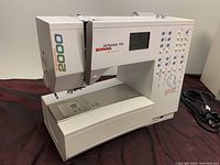 Right-side view of sewing machine showing extended quilting arm, needle plate and foot pedal cable.