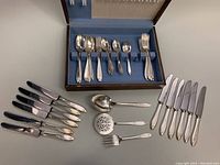 Full flatware set displayed inside and outside of wooden chest showing all forks, knives, spoons, and serving utensils.