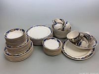 Full view of stacked plates, bowls, teacups, saucers, and platters showing the Johnson Bros Pareek pattern with blue floral border and various sizes.