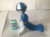 Photo showing battery operated blue and white seal toy holding a blue and white ball on its nose next to a pack of gum for scale.