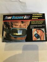 Front view of the product box showing the body building belt device on a waist and partial thigh, with the product name and some features.