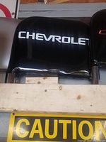 Photo showing the black Chevrolet seat back with white Chevrolet lettering on it, partially obscured by wooden planks in front.