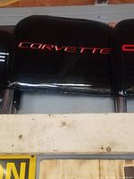Black car seat back with 'CORVETTE' embroidered in red text, showing upholstery and metal supports beneath.