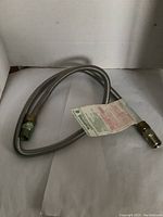 Flexible gas appliance hose with attached warning and installation instructions tag.