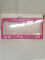 Bright pink license plate frame with white text 'MOVE OVER PRINCESS HERE COMES THE QUEEN' displayed flat against a white background.