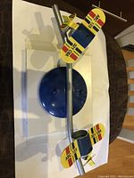 Top-down view of blue round mount with silver arm holding two yellow airplanes with red, blue, and black stripes, laid out on white surface.