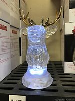 Illuminated clear acrylic stag head figurine with gold-colored antlers on a textured base, lit with white LED light.