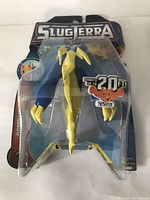 Front view of the toy in original sealed packaging showing yellow winged creature and SlugTerra branding.