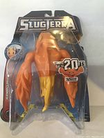 Front view of SlugTerra Burpy toy figure in packaging showing its orange-yellow color and shooting capability up to 20 feet.