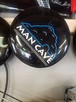 Top view of black round stool cushion with 'MAN CAVE' text and graphic design in white and blue print.