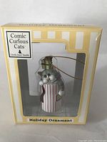 Photo showing curiosity cat ornament inside box labeled Comic Curious Cats by Linda Jane Smith, new in packaging.