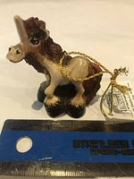 Photo of a vintage new old stock Beasties of the Kingdom unicorn tree ornament with tag. Shows detailed unicorn figure with brown mane, beige body, and attached gold hanging cord.