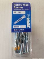 Close-up of a single pack of Sta-Kon Hollow Wall Anchors, showing four metal anchors with yellow tips inside blue and clear packaging.