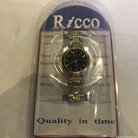 Clear plastic packaging with Ricco quartz wristwatch inside, showing watch face, metal band, and brand card.