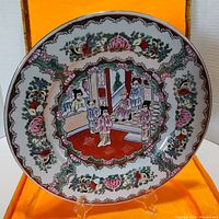 Front view of the Rose Medallion plate showing detailed hand-painted figures and floral border against the orange display box lining.