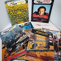 Nine assorted song books and sheet music laid out showing covers with titles and images relevant to genre and era.
