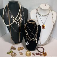 Full view of assorted costume jewelry including necklaces on display busts and earrings, brooches, bracelet on table.