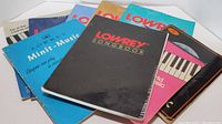Photo showing 8 assorted Lowrey musical instructional and song books with various colorful covers including black, blue, turquoise, pink, and gold.