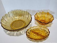 Three amber colored vintage glass pieces: large sunflower bowl, smaller sunflower bowl, and divided thumbprint dish.