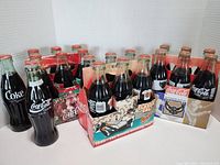 Wide shot showing all five Coca Cola 6 packs with filled bottles featuring sports-themed packaging including Baltimore Ravens, Milwaukee Bucks, Tampa Bay Buccaneers, Baltimore Orioles.