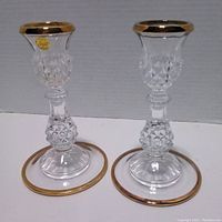 Two Cristal D'Arques lead crystal candlestick holders standing side by side, showing clear crystal with gold trim on top and base.