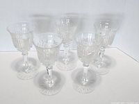Five early 20th century American Brilliant cut glass wine glasses arranged in a group showing clear intricate cut designs on bowls and bases.