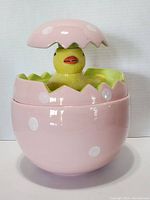 Front view of the pink polka dot ceramic cookie jar with the yellow chick popping out of the cracked egg lid.