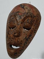 Wooden tribal mask with carved eye and mouth openings, covered in black and red tribal designs.