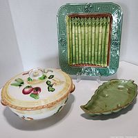 Overall view of three ceramic pottery pieces: Japanese lidded soup tureen with fruit design, Frankoma leaf dish, and California pottery asparagus serving tray.
