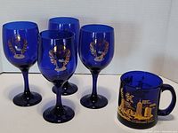 Four cobalt blue Harley Davidson wine glasses and one New York City souvenir mug arranged together, showing front and side views.