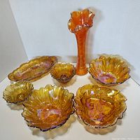 Full lot arranged on white background showing all seven iridescent orange to marigold carnival glass pieces including bowls, vase, candle holders and dishes.