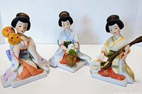 Three vintage bisque porcelain geisha figurines in traditional kimonos with pastel colors, displayed side by side.