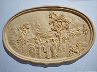 Close-up photo of the tabletop relief carving featuring several figures standing near a cart, trees, and background landscape.