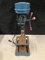 Front view of the drill press showing base, table, and upper head with controls and power cord.