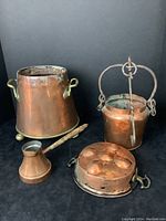 All four antique copper and brass items displayed together on black background: large bucket with brass handles, smaller bucket with iron handle and hanger, Turkish coffee pot, and egg poaching pan