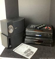 Two Bose speakers stacked next to Sony STR-DE197 stereo receiver and Sony CDP-CE375 CD player; remotes on top; Bose owner’s guide in front.