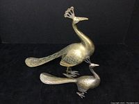 Both brass peacock figurines shown together on a black background to display relative size and detailing.