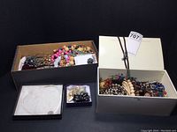 Two open boxes filled with assorted costume jewelry including necklaces, bracelets, earrings, and pins in various colors and materials.