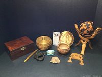 Photo showing all 11 items together including wooden box, carved stone head, woven basket and pen, wooden carved ball on stand, bronze plate, pottery bowl, and small decorative boxes.