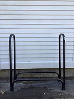 Full view of the black metal firewood rack with tubular tubing and two vertical supports.