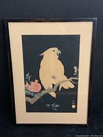 Full view of framed woodblock print depicting a cockatoo on a branch with pomegranates against dark background.