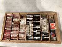 Wooden box with multiple compartments holding over 100 individually packaged diamond needles for turntables, organized in stacks.