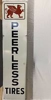 Full-length shot of the rectangular vintage metal sign with PEERLESS TIRES text and griffin logo.