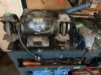 Full view of bench grinder with two grinding wheels and nearby blue vise on workbench