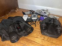 Top view showing 4 cameras and 3 binoculars with their cases on wood floor