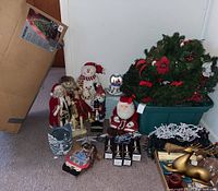 Photo of assorted Christmas decorations including the Noma tree box, figurines such as snowman, Santa, nutcracker, bear, and angel, along with wreaths and lights.