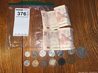 Two folded 1986 Canadian $2 bills with Queen Elizabeth II on front and bird on back alongside an assortment of coins on a wooden table.