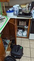 Photo of countertop and stove area with water jug, salad spinner, kitchen scale, baking pans, and small wooden case
