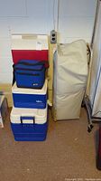 Stacked coolers including large Igloo cooler and smaller coolers with soft-sided cooler on top next to inflatable bed storage bag.